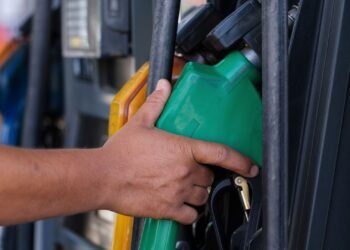 Mão segurando a bomba de gasolina na cor verde em um posto de combustível.