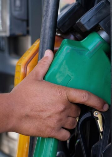 Mão segurando a bomba de gasolina na cor verde em um posto de combustível.