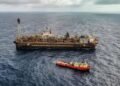 Plataforma de petróleo em operação no mar, acompanhada por uma embarcação de apoio.