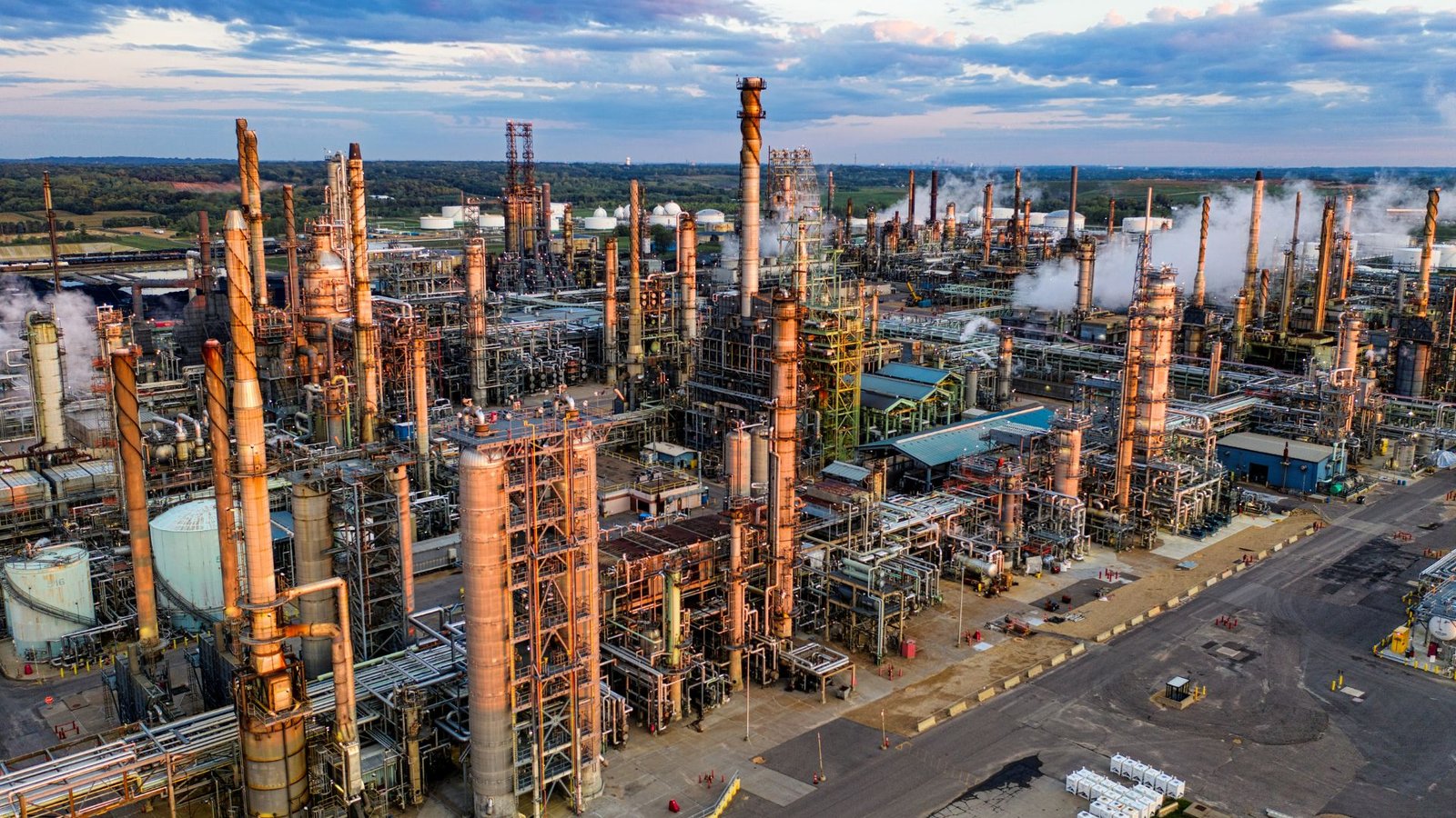 Vista aérea de uma refinaria de petróleo, com torres de processamento, tubulações e estruturas industriais.