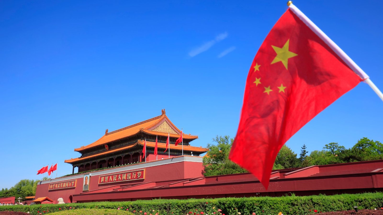 Bandeira da China em primeiro plano, com a Praça da Paz Celestial e o Portão de Tiananmen ao fundo, em Pequim.